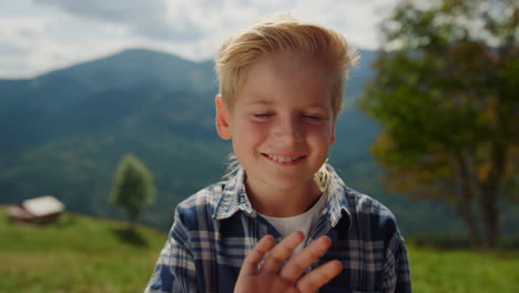 smiling boy waving hand on green meadow close up. portrait of happy little man.