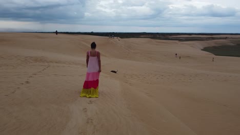 Mujer-Con-Vestido-Colorido-Camina-Con-Perro-En-Una-Duna-De-Arena,-Santa-Cruz-Bol