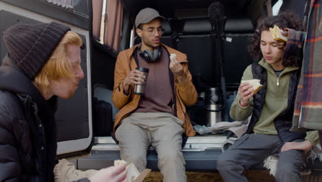 a movie production team taking a break while eating a sandwich and talking behind a van in the street 5