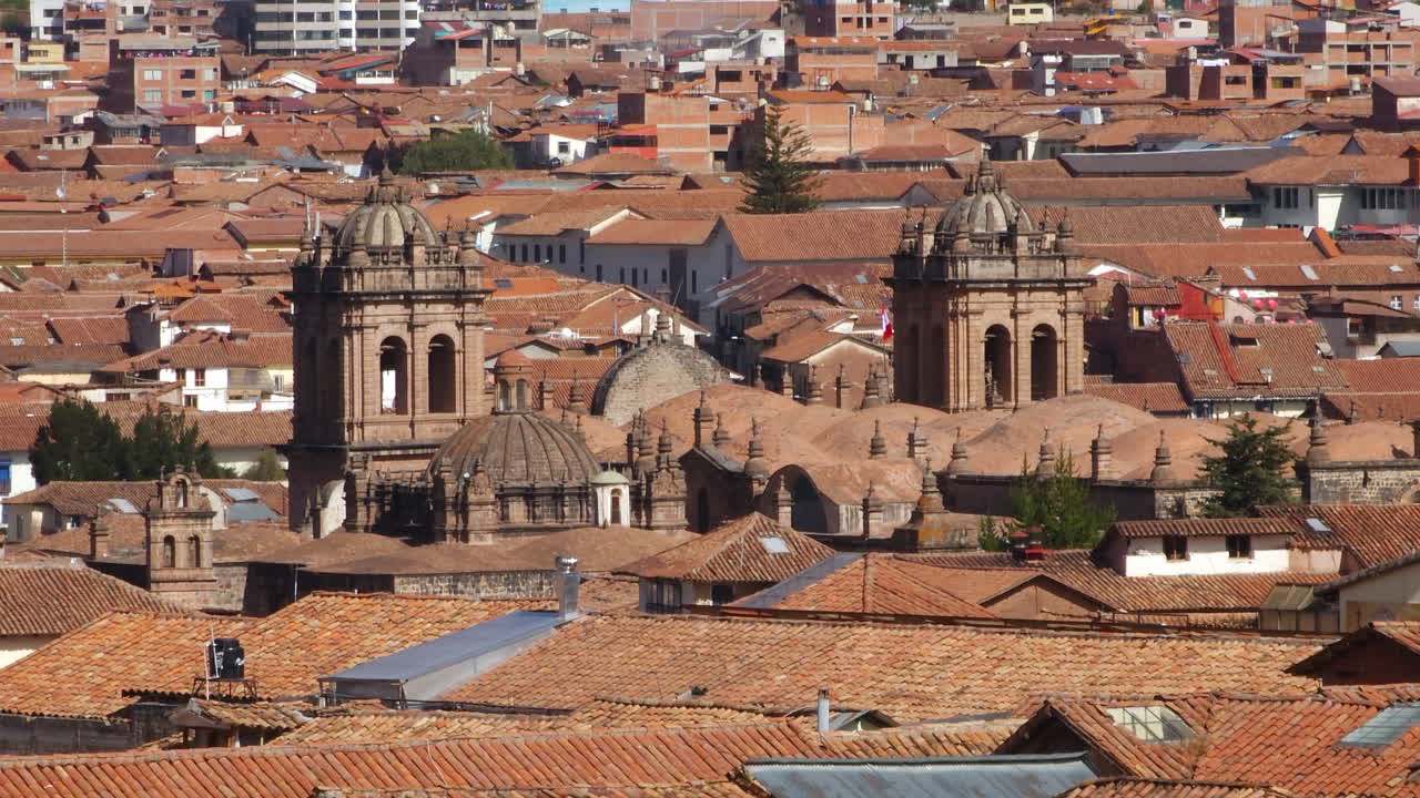 Unique tiled rooftops and beautiful colonial church domes in Cusco's historic center. The footage showcases the city's charming architecture against the Andes Mountains