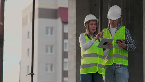 Un-Trabajador-De-La-Construcción-Y-Una-Arquitecta-Con-Casco-Discuten-El-Plan-De-Construcción-De-La-Casa-Y-Se-Cuentan-Sobre-El-Diseño-Sosteniendo-Una-Tableta,-Miran-El-Fondo-De-Los-Dibujos-De-Los-Rayos-Del-Sol.