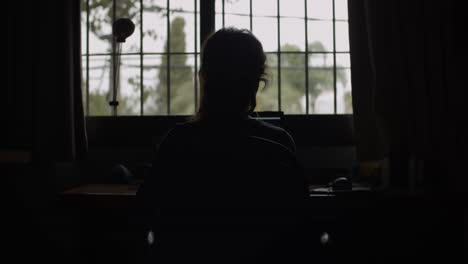 4k at 24fps - woman on the computer on a rainy day with backlight - mistery mood