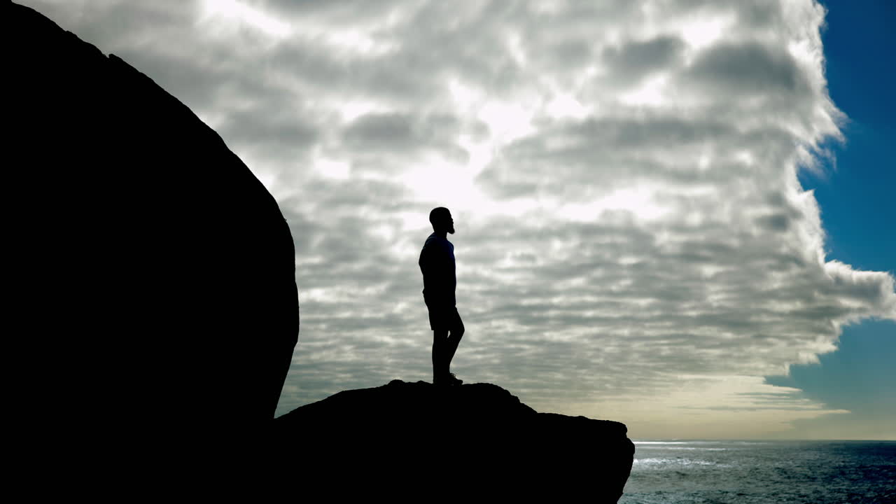 Silhouette of a man standing on a cliff overlooking the ocean
