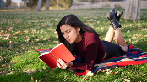 una linda estudiante universitaria leyendo un libro al aire libre en el parque antes de que comience la clase en el semestre de otoño