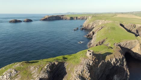 An-aerial-view-of-Abereiddi-Tower-in-Pembrokeshire,-South-Wales,-on-a-sunny-evening-with-a-clear-blue-sky