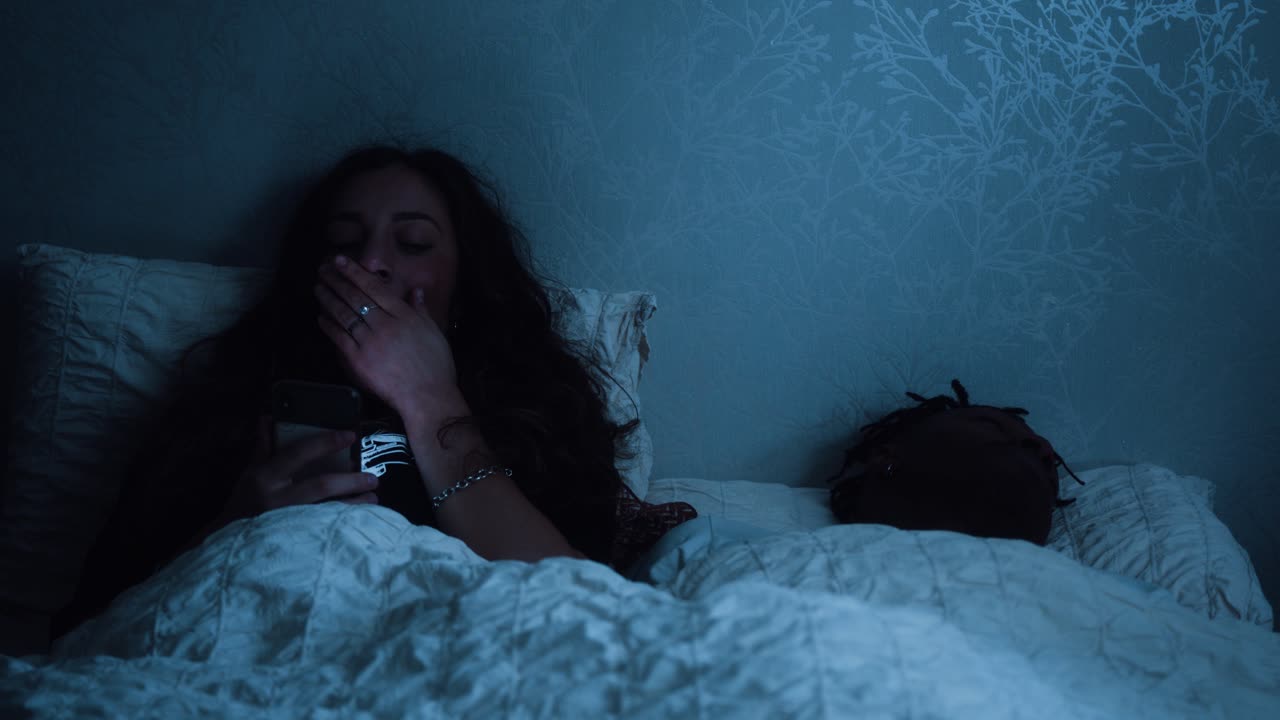 mujer cansada bostezando mientras usa su teléfono inteligente tarde en la noche en la cama