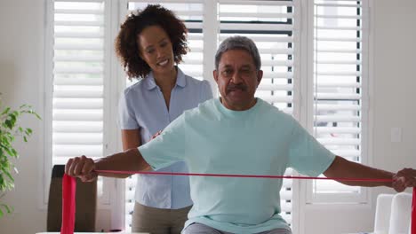 Mixed-race-female-physiotherapist-helping-senior-man-exercise-using-exercise-band