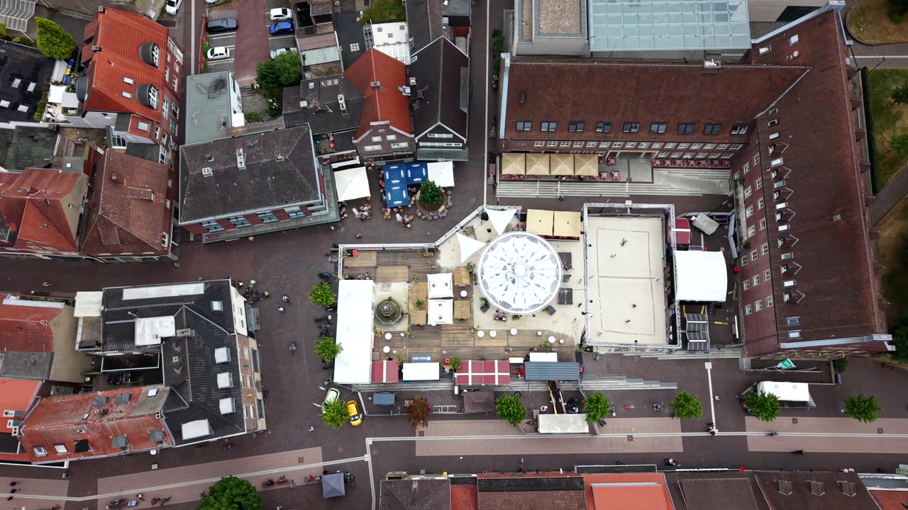 Een zandvolleybalveld staat centraal op het stadsplein van Dülmen, Noordrijn-Westfalen, Duitsland, met daken van rode pannen en buitenmarktkramen rondom het levendige evenementenplein. Luchtopname met drone van bovenaf.