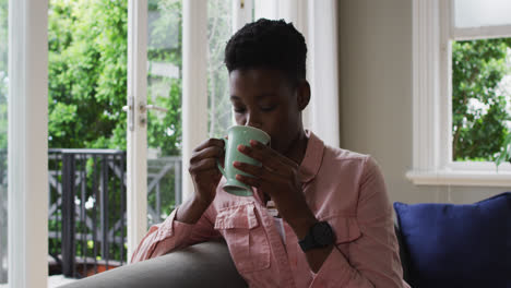 african american woman drinking coffee while sitting on the couch at home