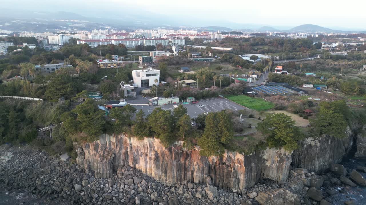 Drone aerial view in South Korea near a cliff with green trees over rocky area parking lot jeju island