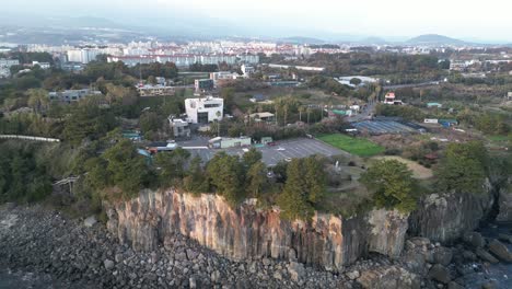 drone aerial view in south korea near a cliff with green trees over rocky area parking lot jeju island