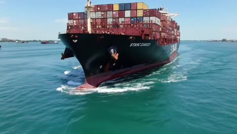 massive cargo ship navigating through calm waters, displaying a rainbow of shipping containers against a clear blue sky in a breathtaking maritime scene