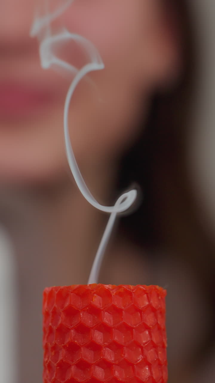 primer plano de una vela roja que emite un delicado humo después de extinguirse, con figuras borrosas en el fondo observando, la suave brisa de humo se eleva