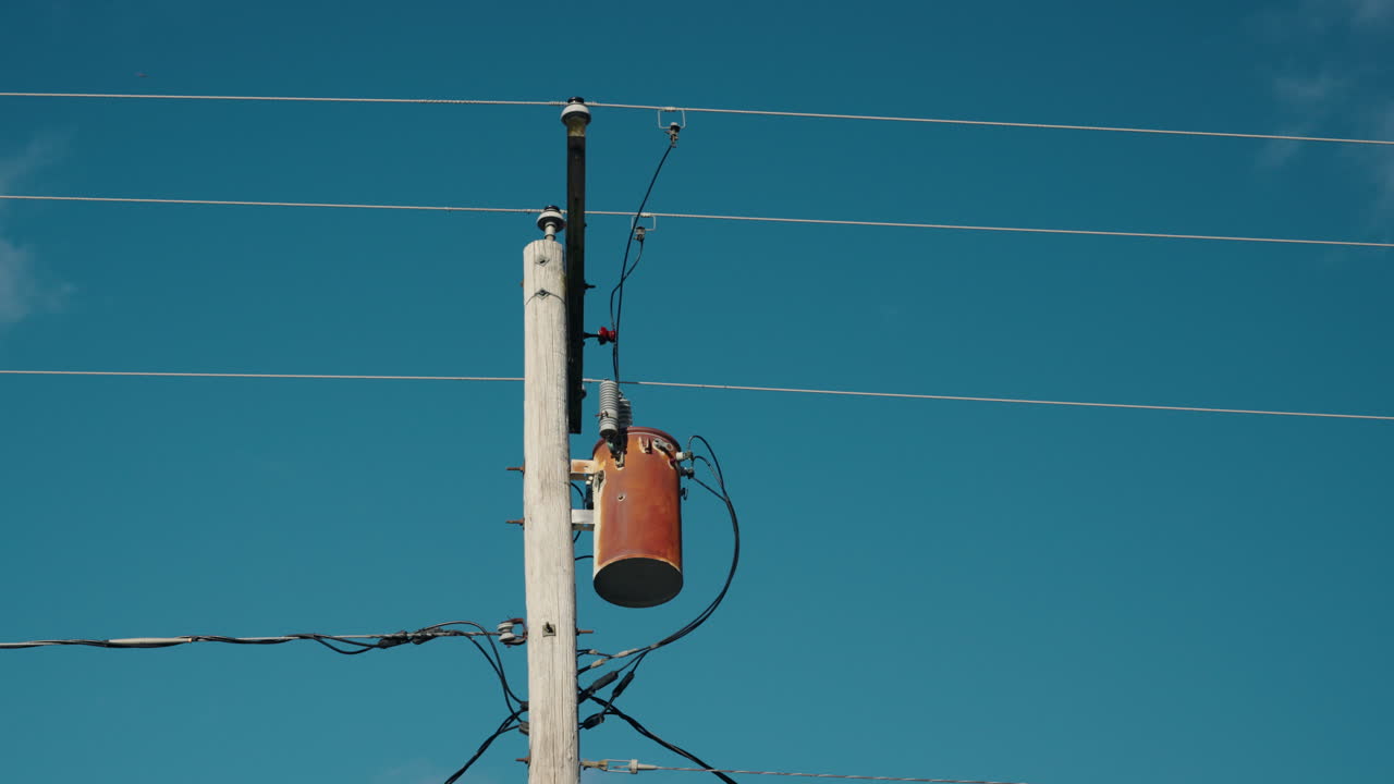 Wooden utility pole with transformer and power lines against clear blue sky, electrical infrastructure in outdoor environment