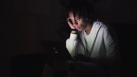 serious young man sitting on couch and using laptop at night