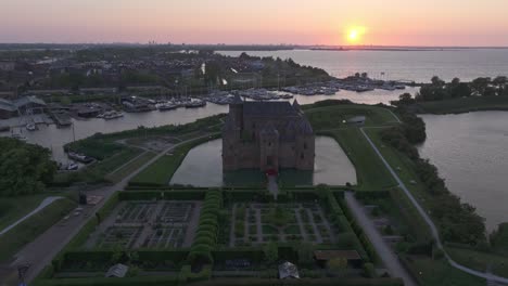 Flying-backwards-at-medieval-castle-Muiderslot-during-sunset,-aerial