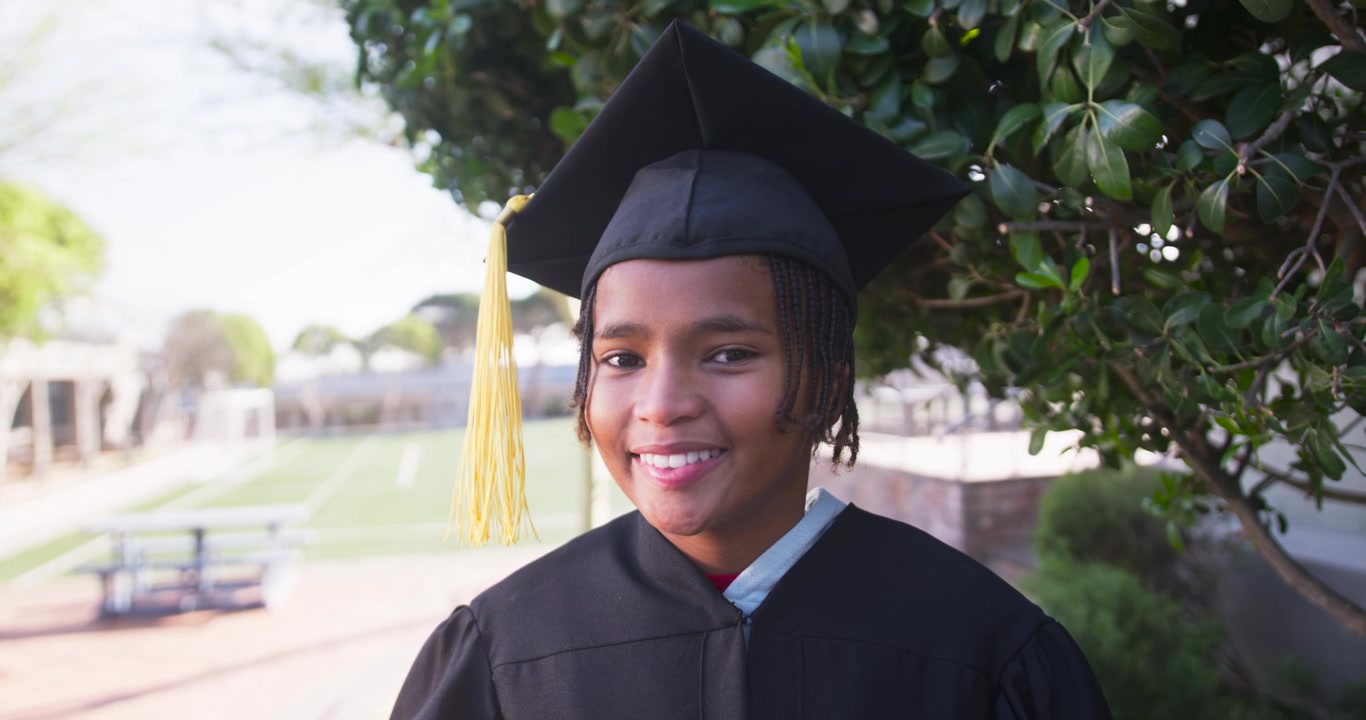 Grabando a un adolescente afroamericano posando para su graduación en el patio de la escuela, sonriendo y girando hacia la cámara, con toga y borla.