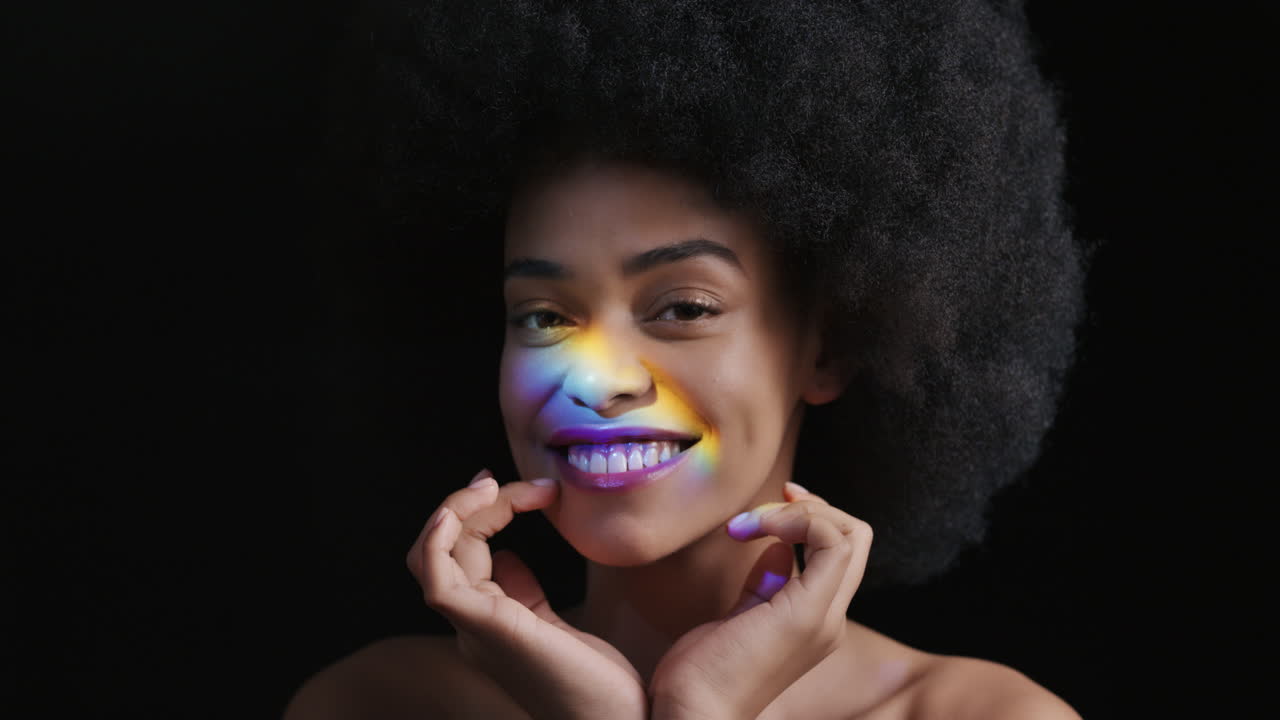 retrato multicolor de cerca hermosa mujer afroamericana con afro disfrutando de una piel suave y saludable con aspecto confiado belleza natural luz colorida sobre fondo negro concepto de cuidado de la piel