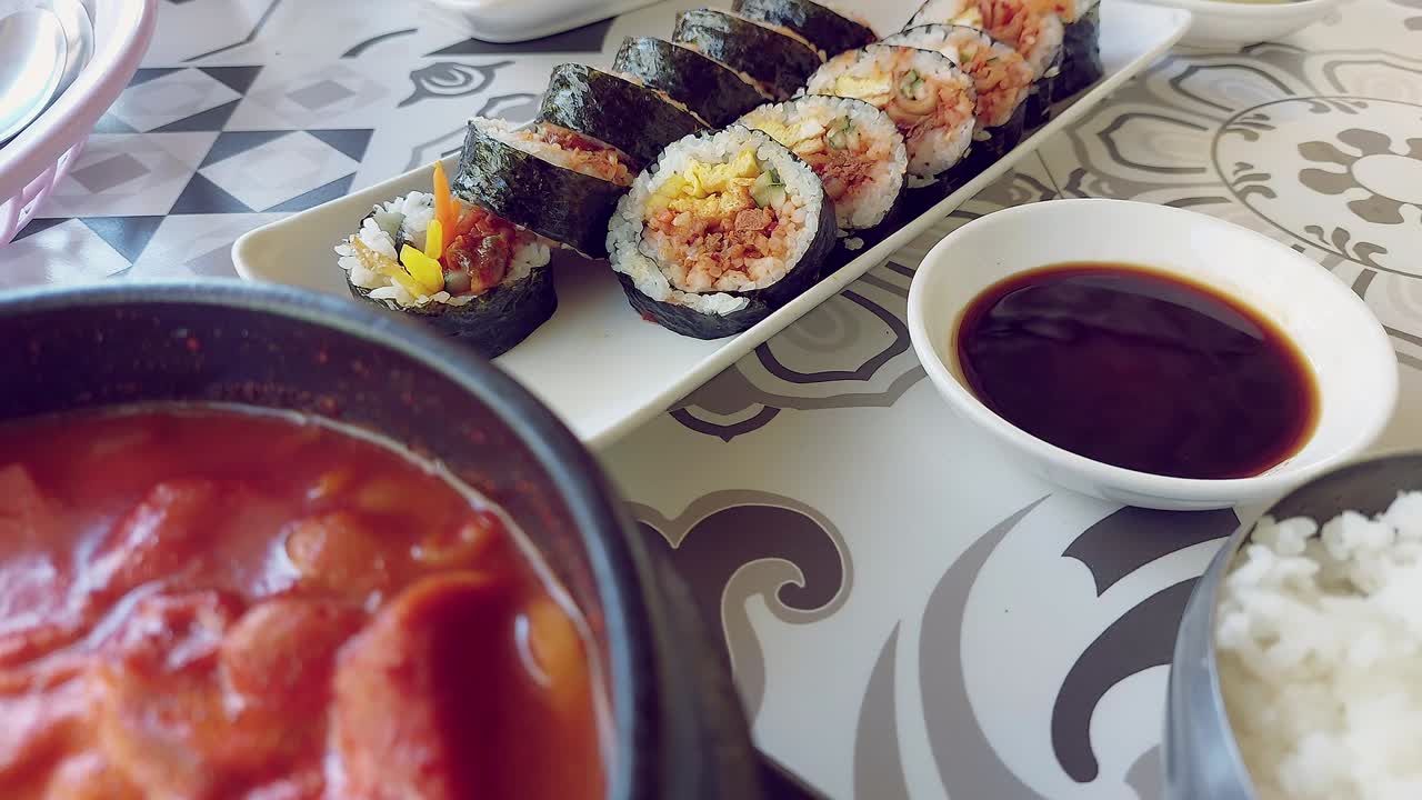 Candid restaurant scene of dipping a slice of kimchi gimbap or seaweed rice roll in soy sauce, authentic traditional local Korean food