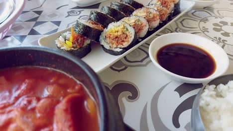 candid restaurant scene of dipping a slice of kimchi gimbap or seaweed rice roll in soy sauce, authentic traditional local korean food