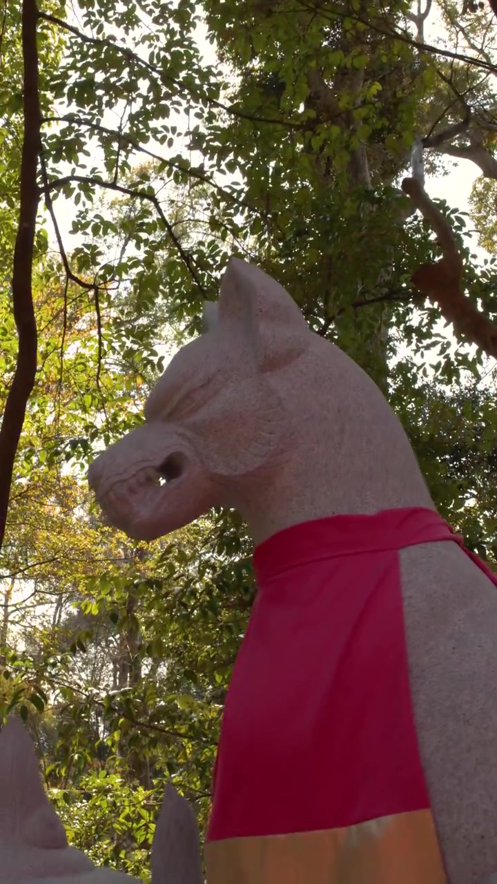 Tomada em ângulo baixo de uma escultura de raposa de pedra usando um babador vermelho contra árvores da floresta.