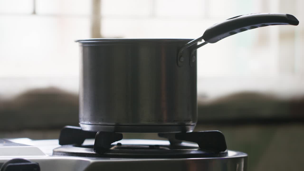 A metal pot on a stovetop, and a hand rotates a switch in slow-motion against blur background
