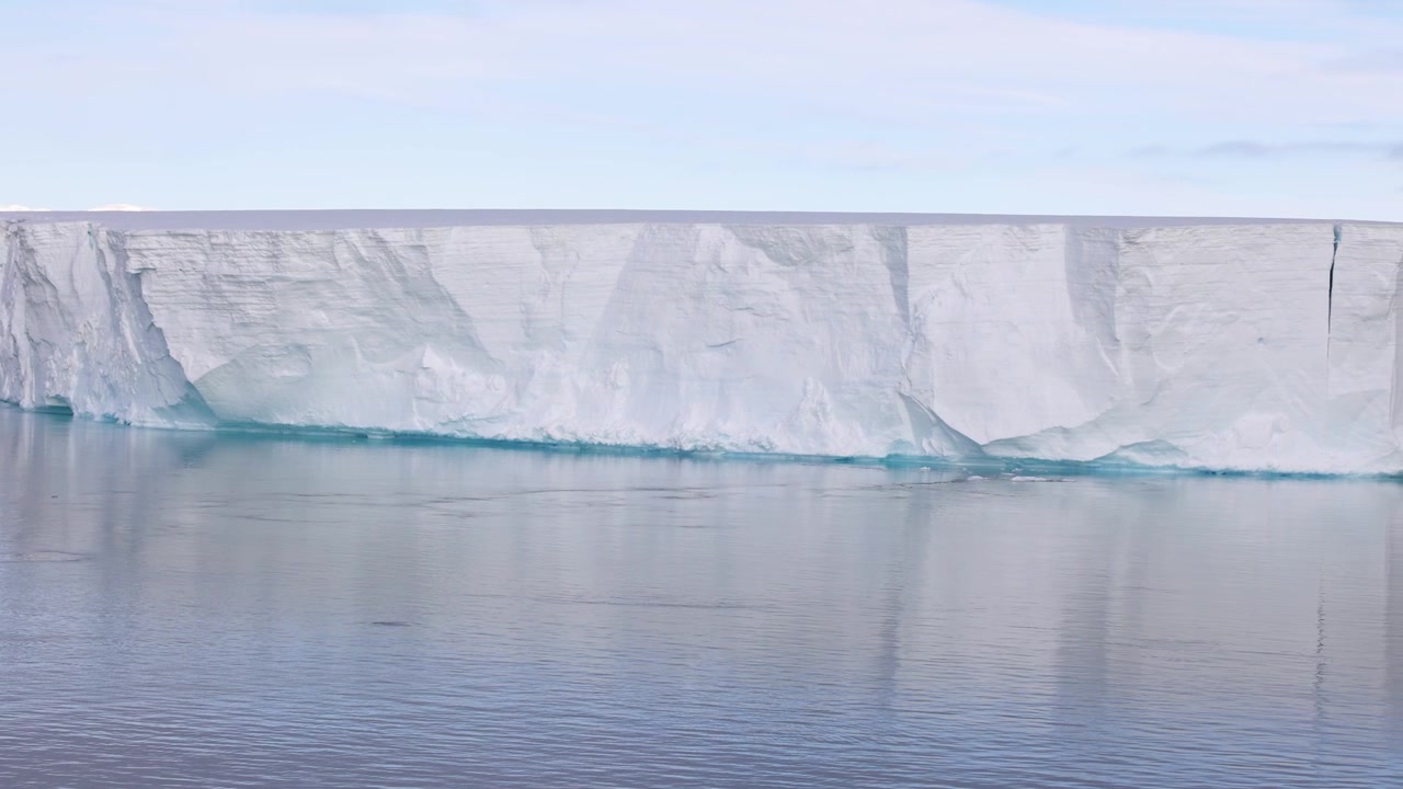 Huge tabular iceberg floating on calm seas near the Antarctic Peninsula. Vast ice formation reflecting in still water, highlighting polar wilderness and climate themes