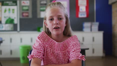 Portrait-of-causacian-schoolgirl-sitting-at-classroom,-answering-question,-looking-at-camera