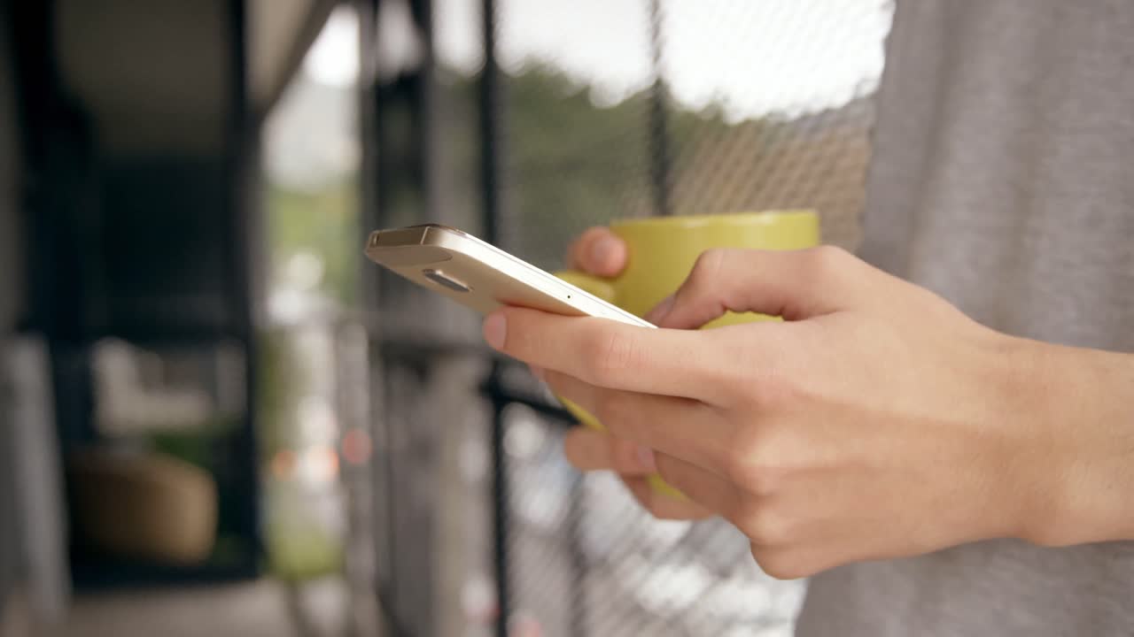 hombre usando teléfono móvil mientras sostiene una taza de café en casa 4k
