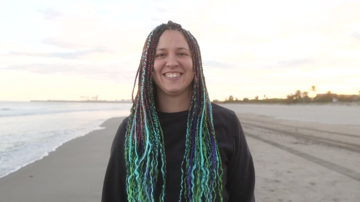 una donna con le trecce ride guardando la telecamera al tramonto sulla spiaggia