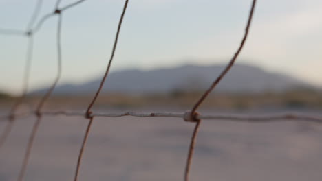 close up of a rusty metal fence along a field, through which mountains can be seen in the distance