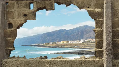 Looking-through-large-hole-in-the-wall-towards-the-town-near-the-sea,-static-handheld