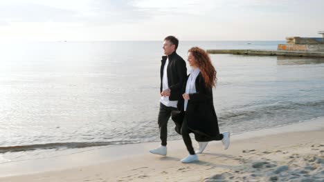 young couple running on the sandy beach. pair having fun, fooling, holding hands, enjoying moment. romantic sunset during spring travel vacation holiday honeymoon. playful girl and man in love