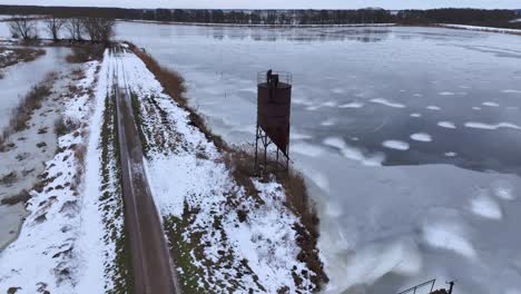 an aerial view of an old, rusty, metal fish-feeding tower, standing by a large body of water in wintertime. europe lithuania.