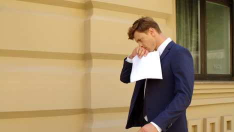 Thoughtful-business-man-walking-with-financial-documents-outdoors