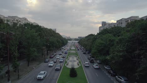 Luftaufnahme-über-Den-Unirii-Boulevard-In-Bukarest,-Rumänien-In-Der-Abenddämmerung,-Langsame-Aufwärtsbewegung,-Wasserfontänen,-Unten-Vorbeifahrende-Autos,-Hohes-Gebäude