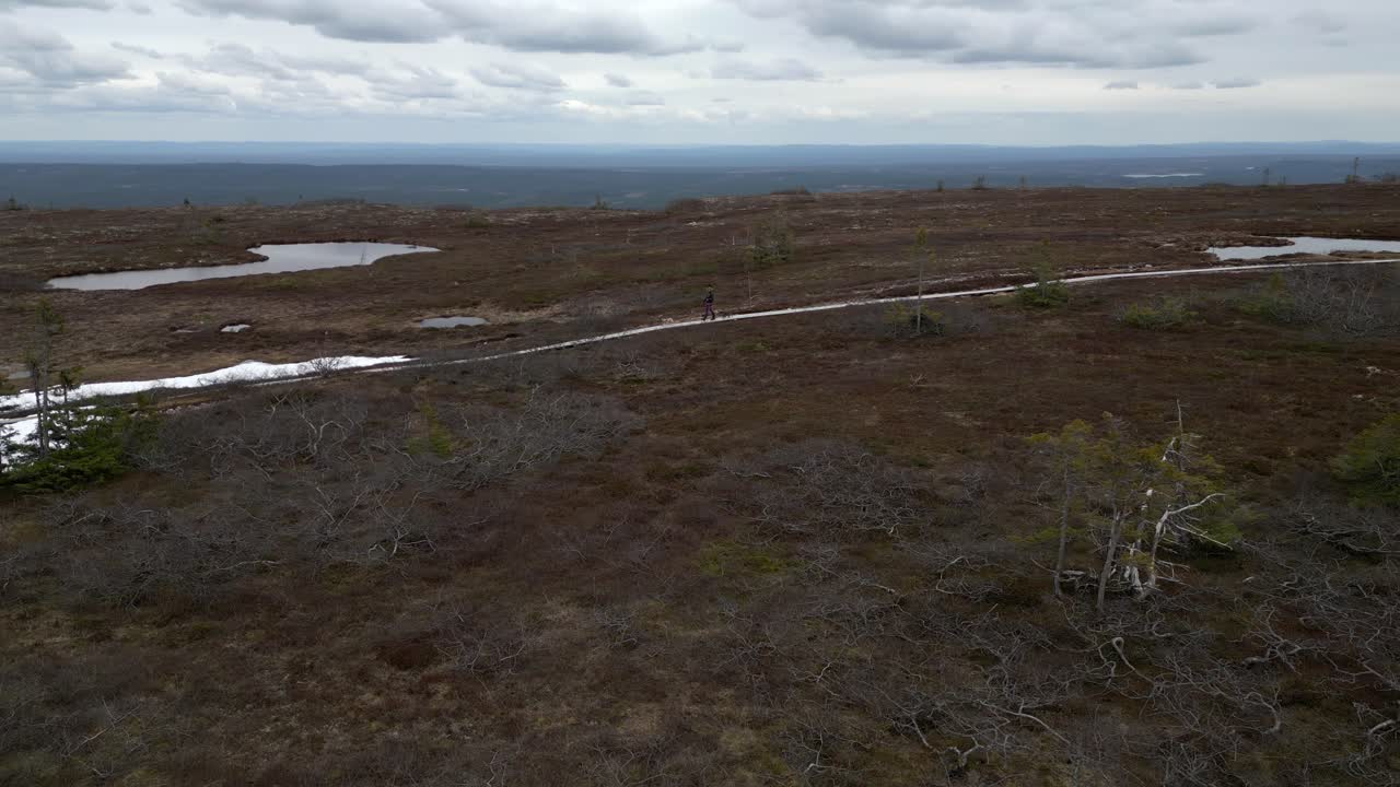 una mujer y su bulldog francés caminando por un camino de grava de montaña con un pequeño lago detrás de ellos