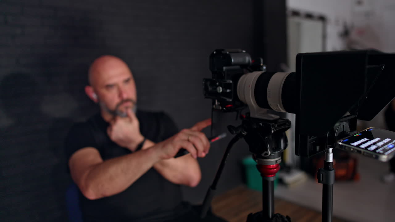 Male Caucasian photographer sits looking at the display of camera. Portrait of a cameraman working in studio.