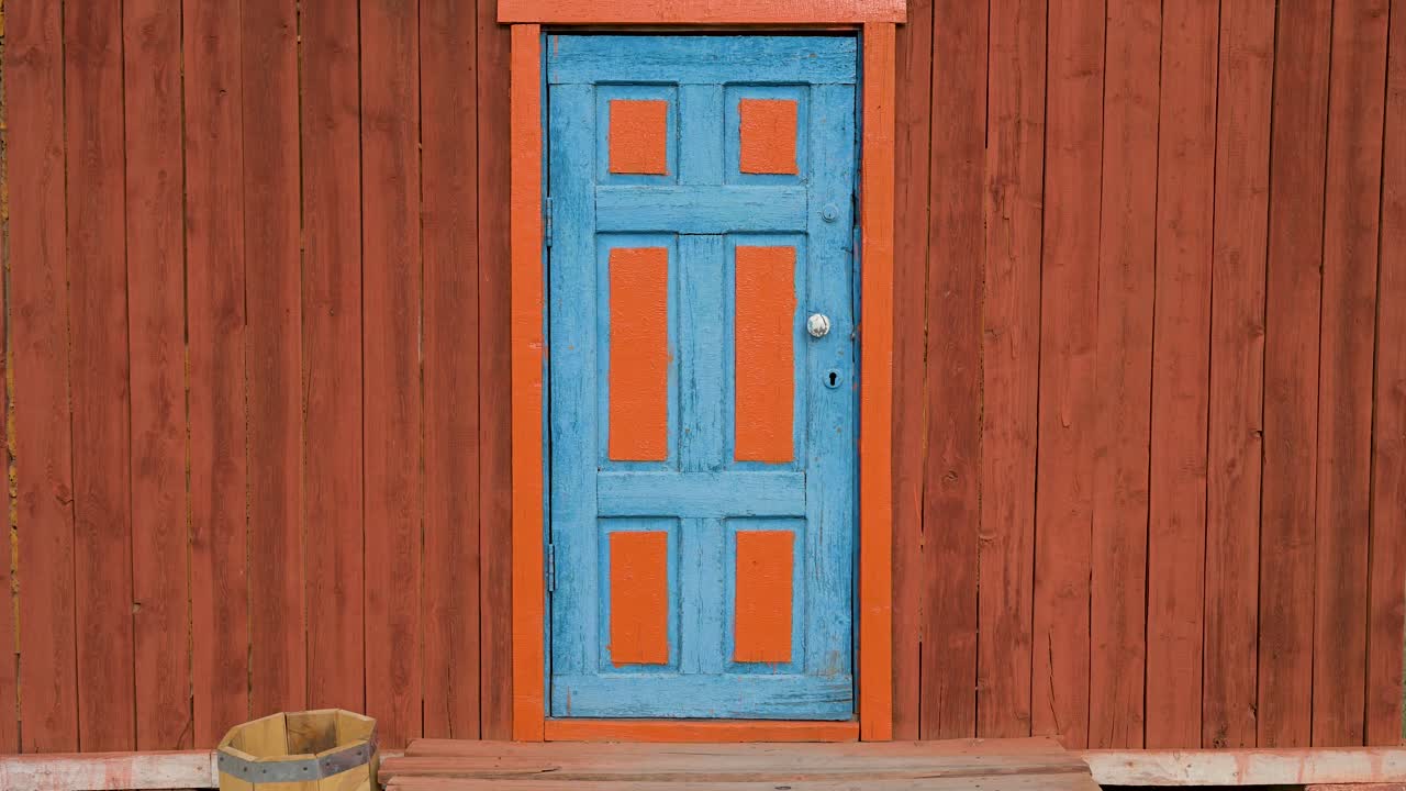 A blue and orange door in a wooden wall