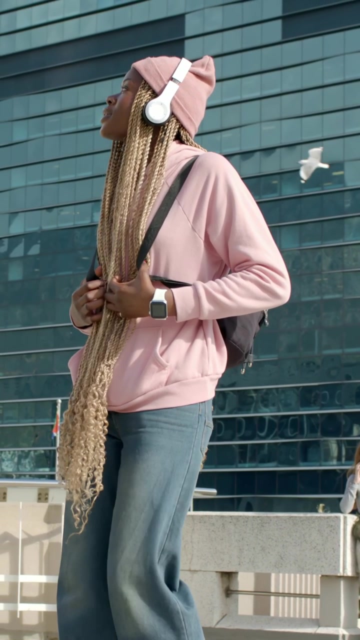 Vertical video: Walking woman in pink hoodie and beanie with pack on urban walkway watching seagull