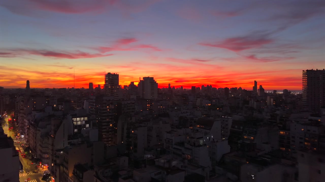La telecamera si muove sopra edifici cittadini oscurati verso un cielo vibrante rosso e arancione
