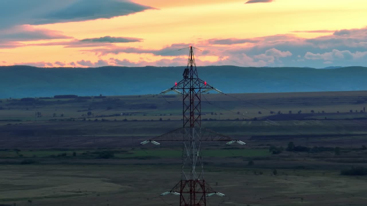 Aerial view showing electricity pylon on rural field in front of hills at sunset