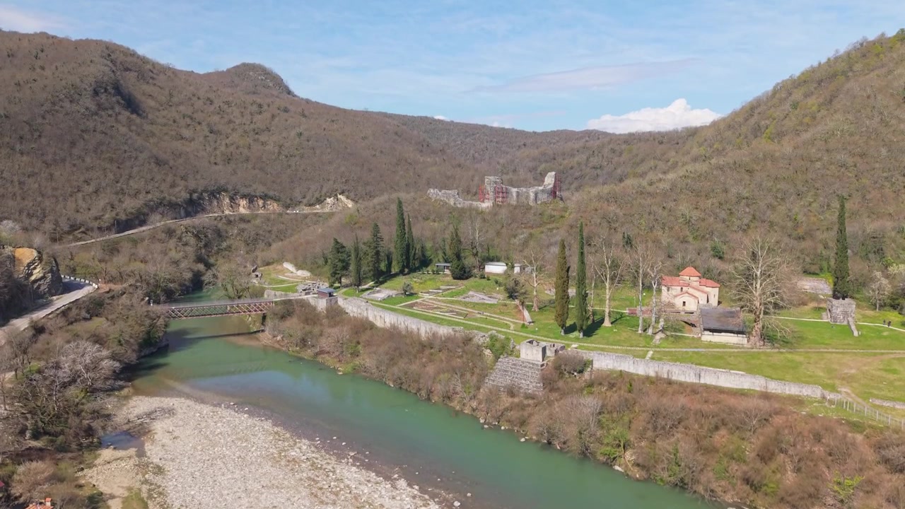 Elevazione drone che rivela l'antica Fortezza di Nokalakevi, circondata da una natura verde e rigogliosa e un fiume serpeggiante che scorre attraverso lo scenografico paesaggio georgiano