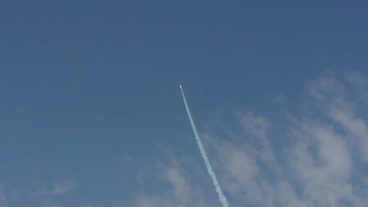 A small rocket launches from a remote desert testing facility into the blue sky leaving a prominent white smoke trail