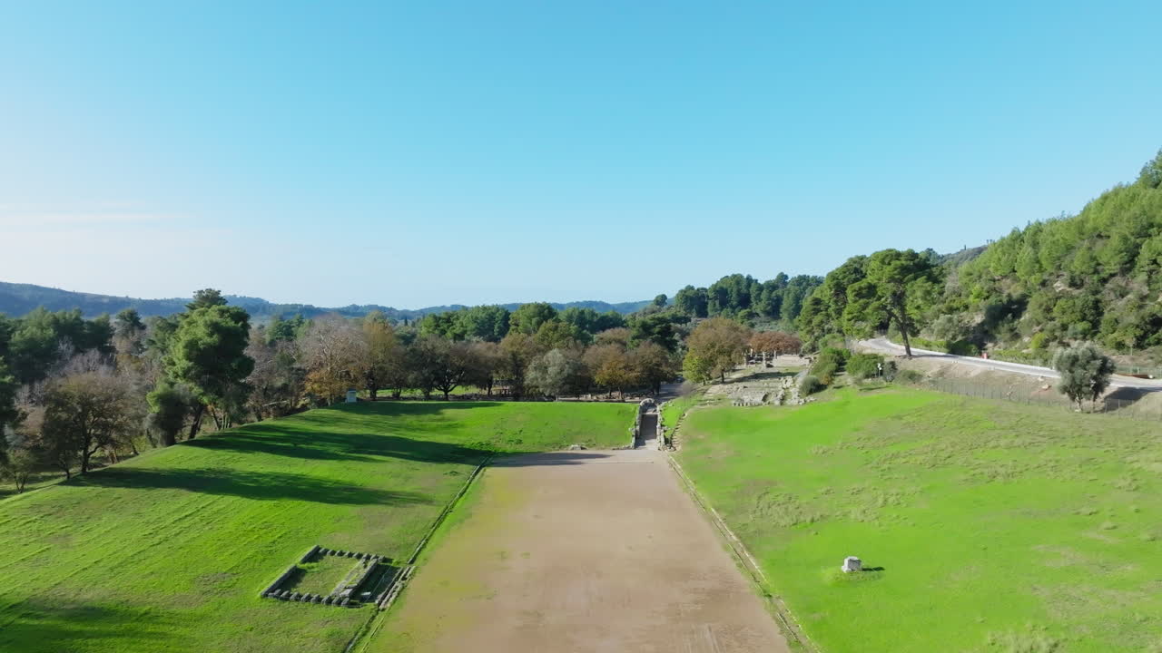 Drone flyover of the ancient stadium track at Olympia, nestled in the green heart of the Peloponnese and framed by remnants of classical temples and trees in bloom