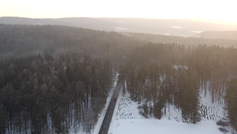 Toma-Aérea-De-Un-Auto-Conduciendo-A-Través-De-Un-Bosque-Cubierto-De-Nieve-Al-Atardecer,-Hermosa-Escena-Invernal