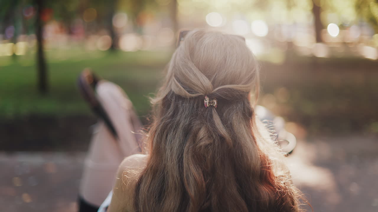 A mother with long wavy hair siting on a bench, breastfeeding her baby in a peaceful park, next to a modern baby stroller