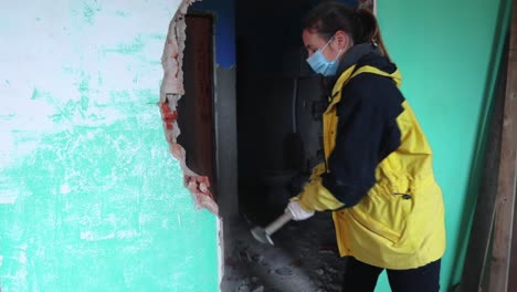 mujer fuerte con máscara médica demoliendo un muro de hormigón aplastándolo con un mazo - plano medio