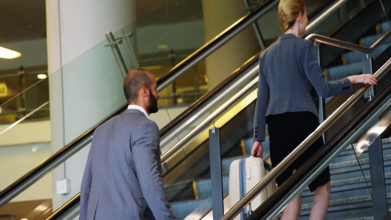 Empresário e empresária subindo a escadaria com bagagem