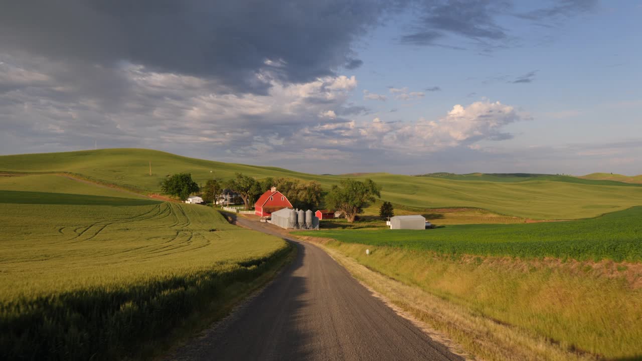 Scenic aerial footage of a tranquil farmstead nestled in lush, rolling hills under dramatic skies in England's Lake District. Captured in golden hour, showcasing serene rural beauty